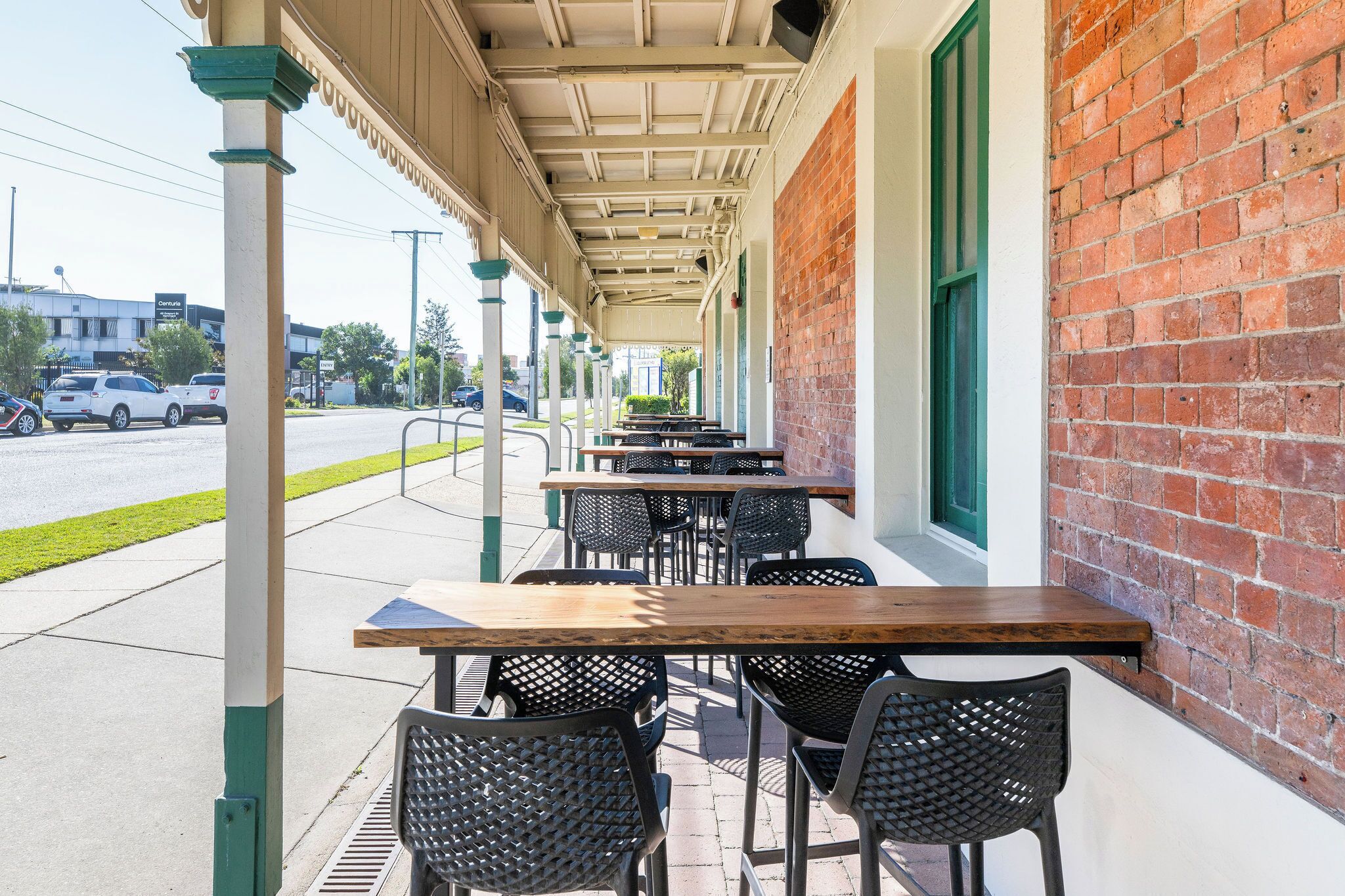 An outdoor patio with tables and chairs, a brick wall, and a covered walkway.