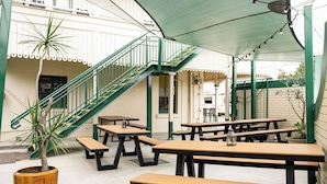 An outdoor patio area with multiple wooden picnic tables, a staircase with green railings, and a potted plant.