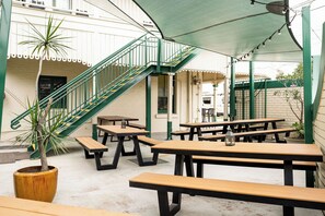 An outdoor patio area with multiple wooden picnic tables, a staircase with green railings, and a potted plant.