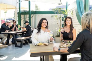 An outdoor dining area with tables and chairs, a brick wall, and greenery in the background. - Queensport Hotel (Brisbane)