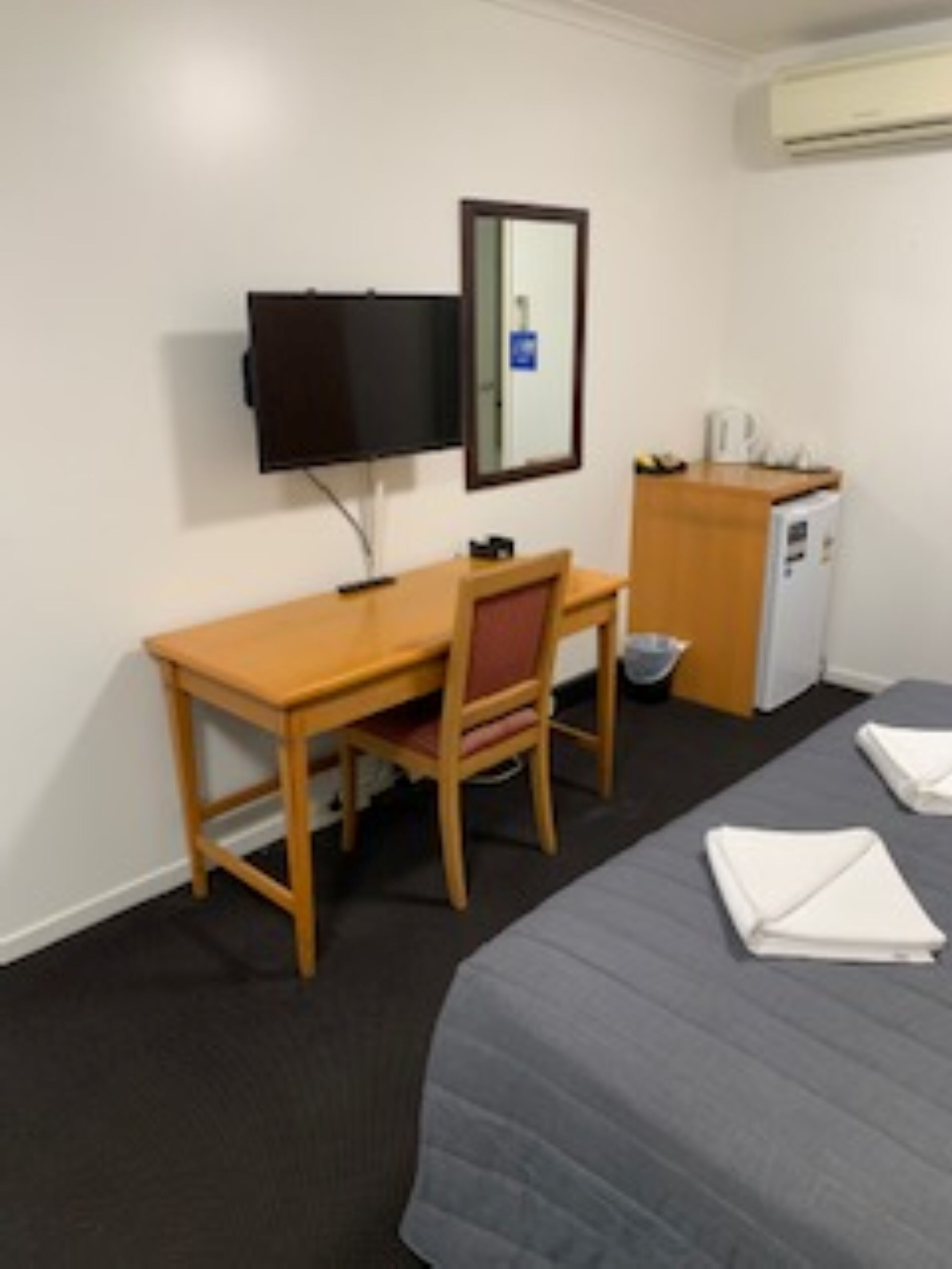 Hotellihuone, jossa on sänky, työpöytä, tuoli, televisio, pieni keittokomero ja peili.
