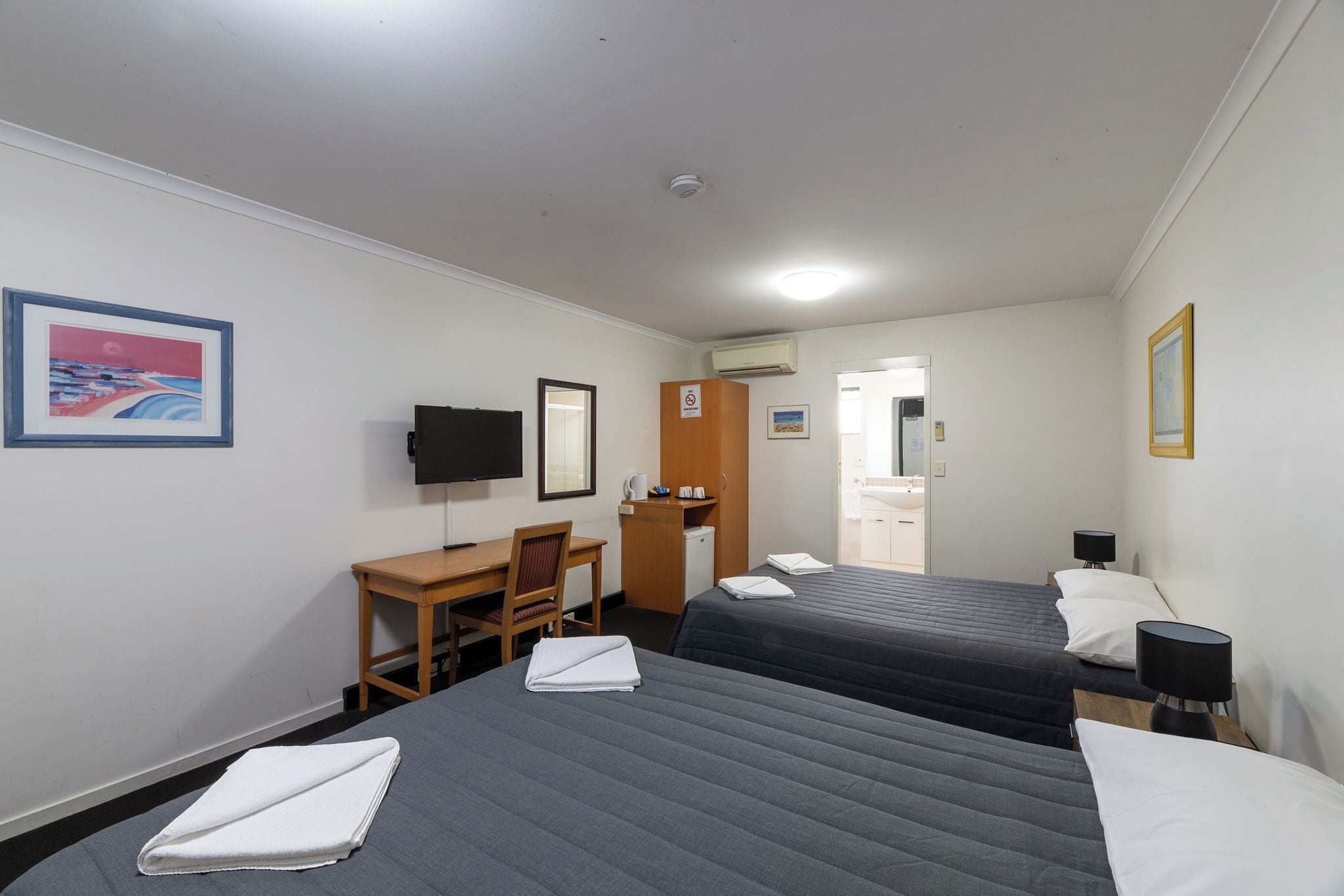 Ett hotellrum med två sängar, ett skrivbord, en stol, en tv och ett badrum som syns genom en öppen dörr.