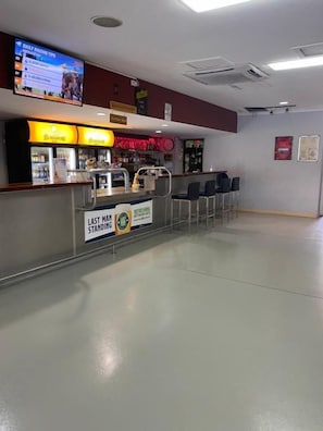 Uma área de bar com balcão, assentos e uma tela de televisão.