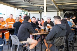 Un grupo de personas sentadas en mesas bajo una estructura cubierta, presumiblemente un espacio de comida informal o para socializar.