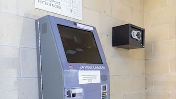 A 24-hour check-in kiosk at the Queensport Hotel & Motel with a map and a security camera above it.