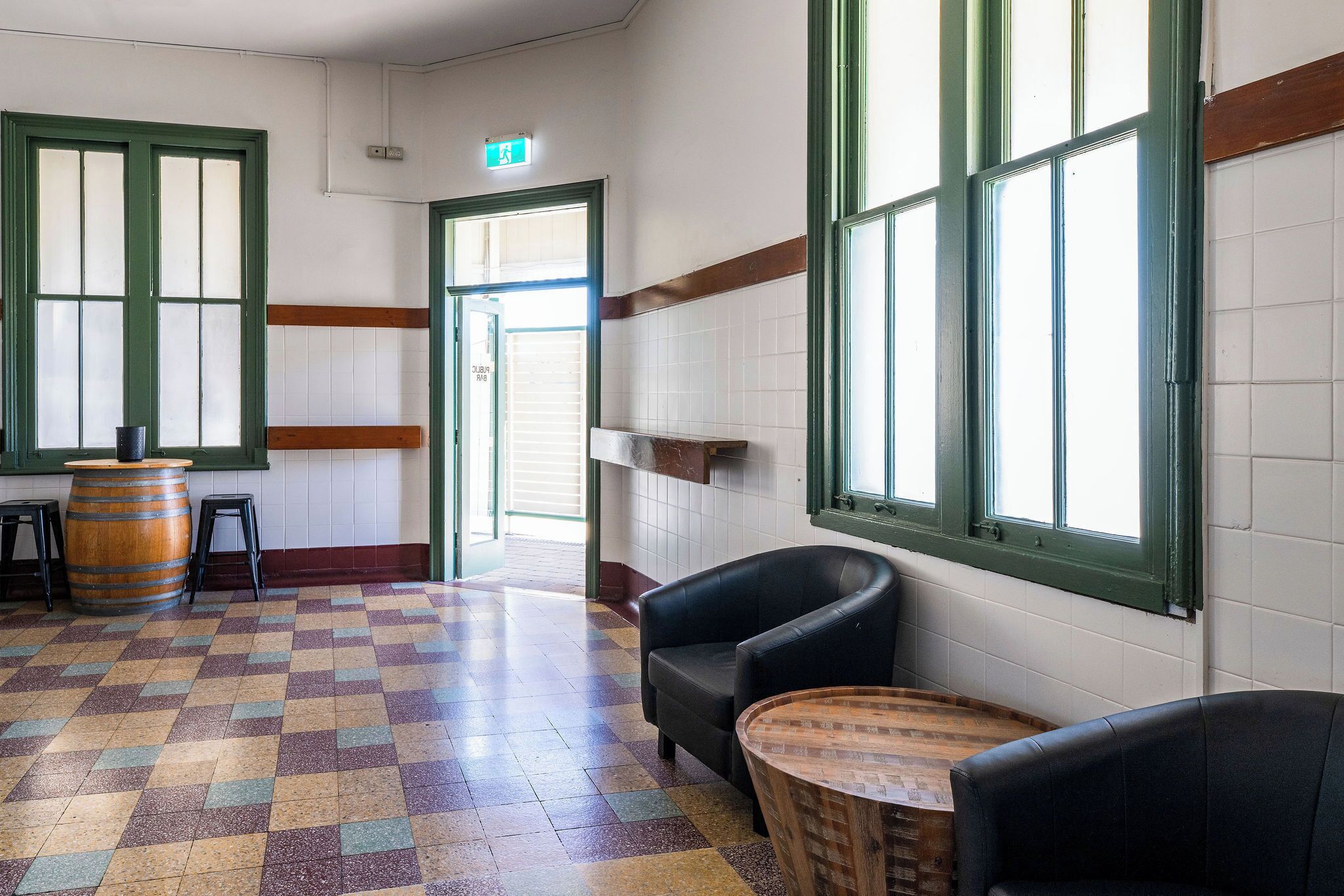 A room with a checkered floor, a wooden barrel, two black chairs, and a round wooden table.
