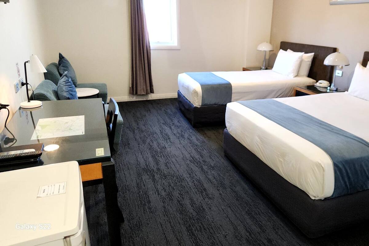 Habitación de hotel con dos camas, un escritorio con computadora, una silla y una ventana con cortinas.