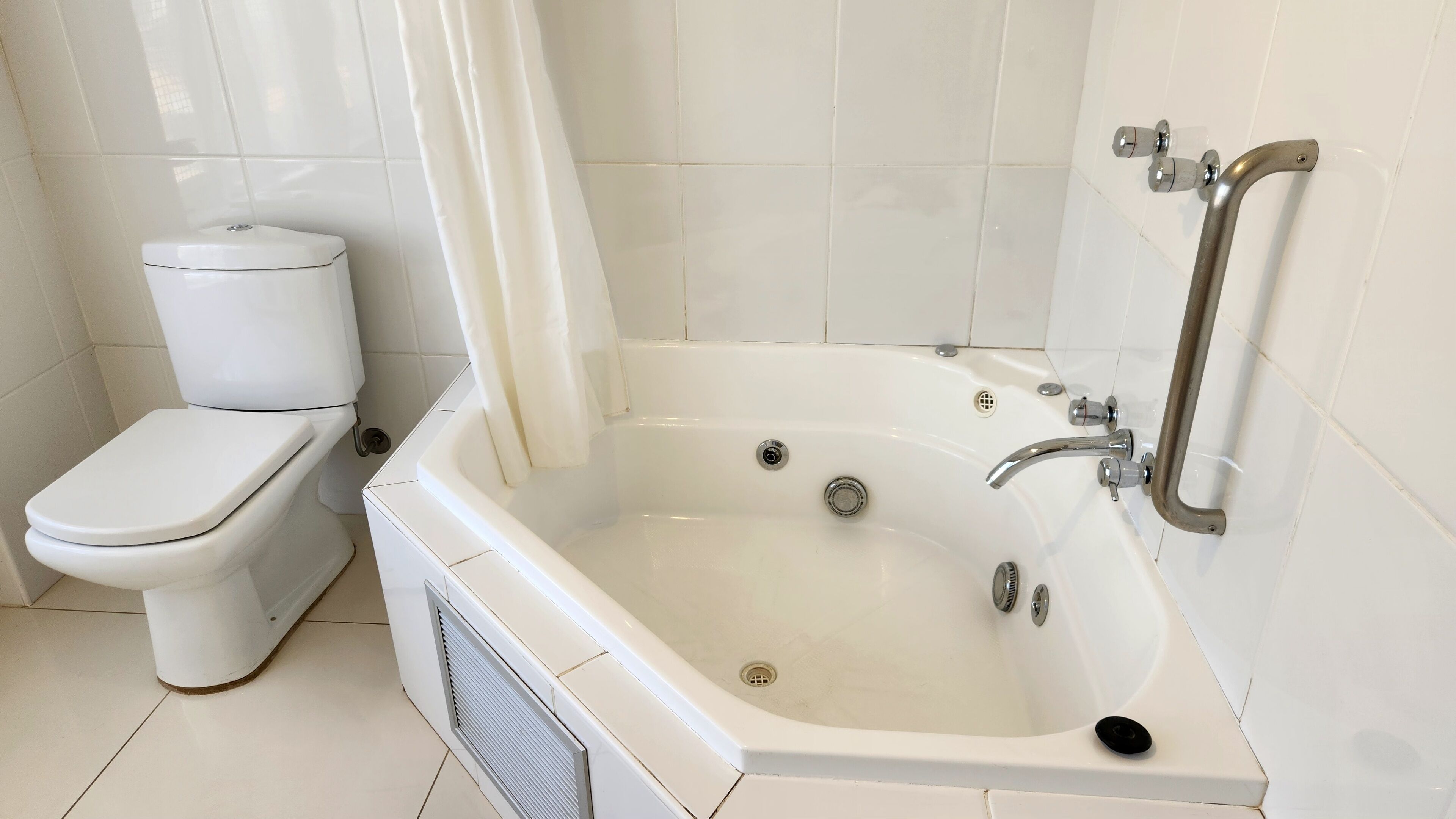 A bathroom with a white toilet, a bathtub with a shower curtain, and a handrail.