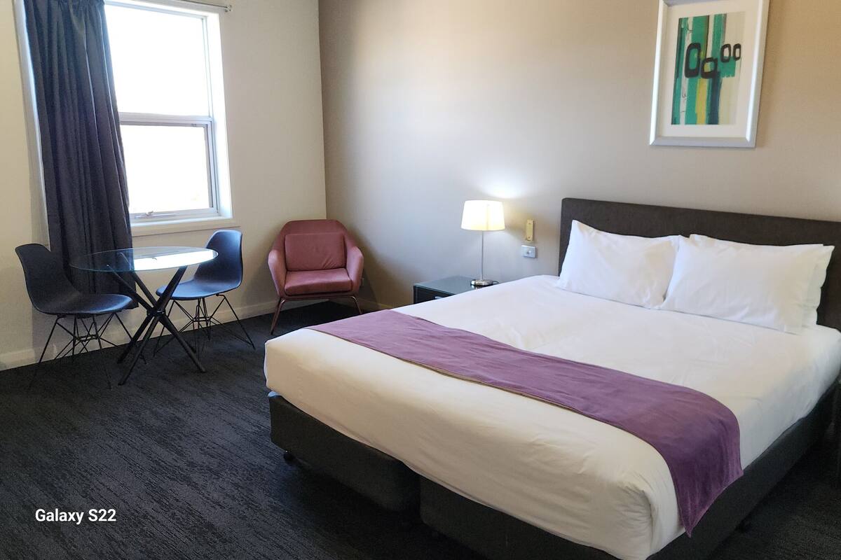 Una habitación de hotel con una cama grande, un escritorio con silla, una mesita y dos lámparas.