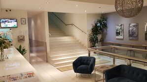 A modern hotel lobby with a staircase, seating area, and artwork on the walls.