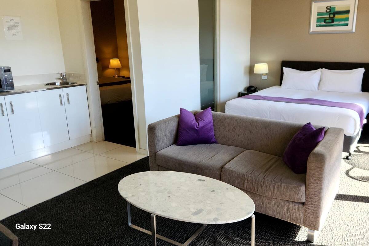 Habitación de hotel con sofá, mesita, cama y baño visible a través de una puerta abierta.