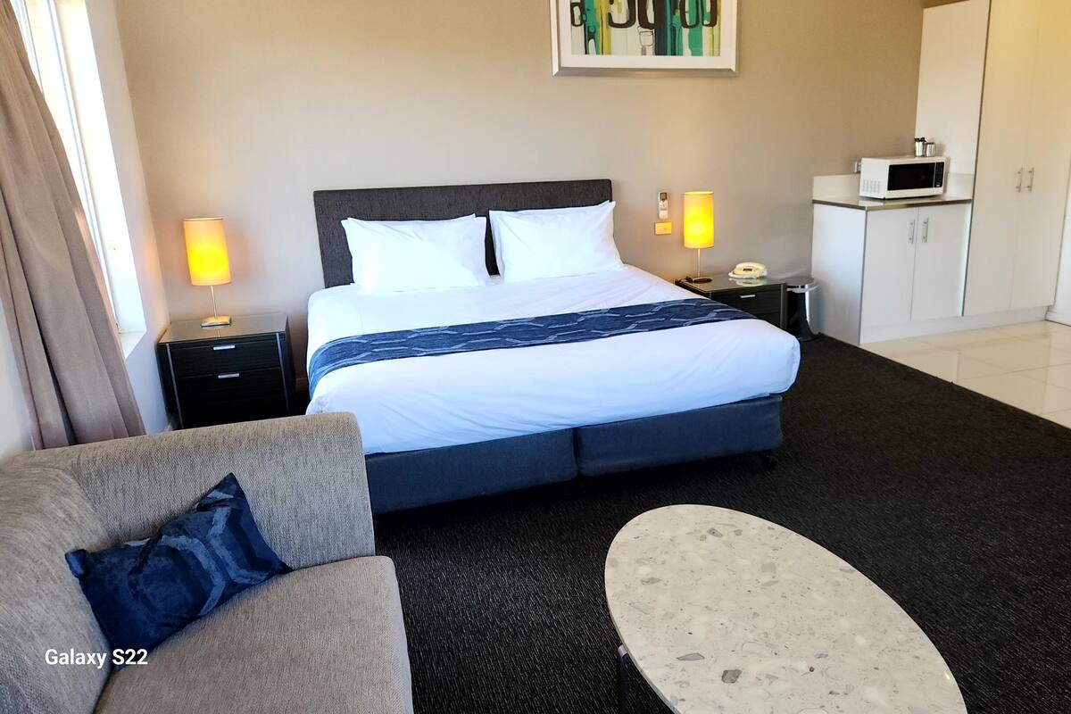 Habitación de hotel con cama Galaxy S22, sofá, una mesita pequeña, microondas y un armario.