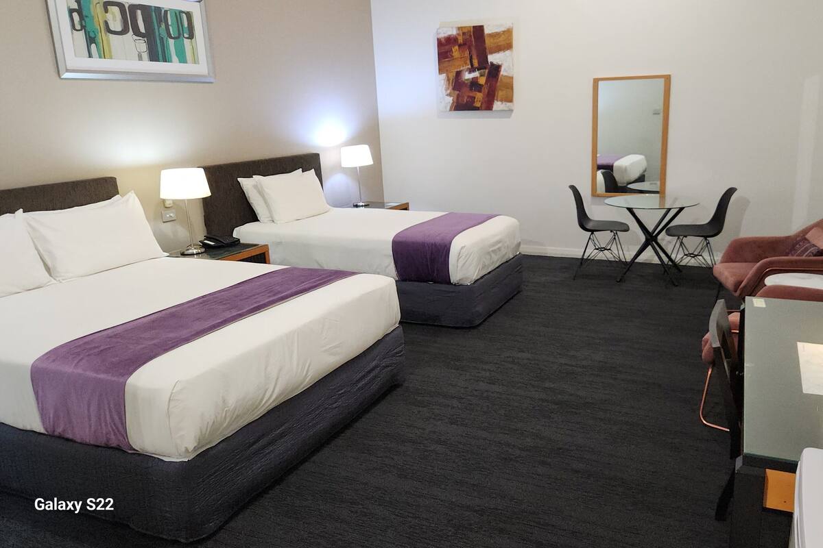 Una habitación de hotel con dos camas, un escritorio, una silla, una mesita y un espejo.
