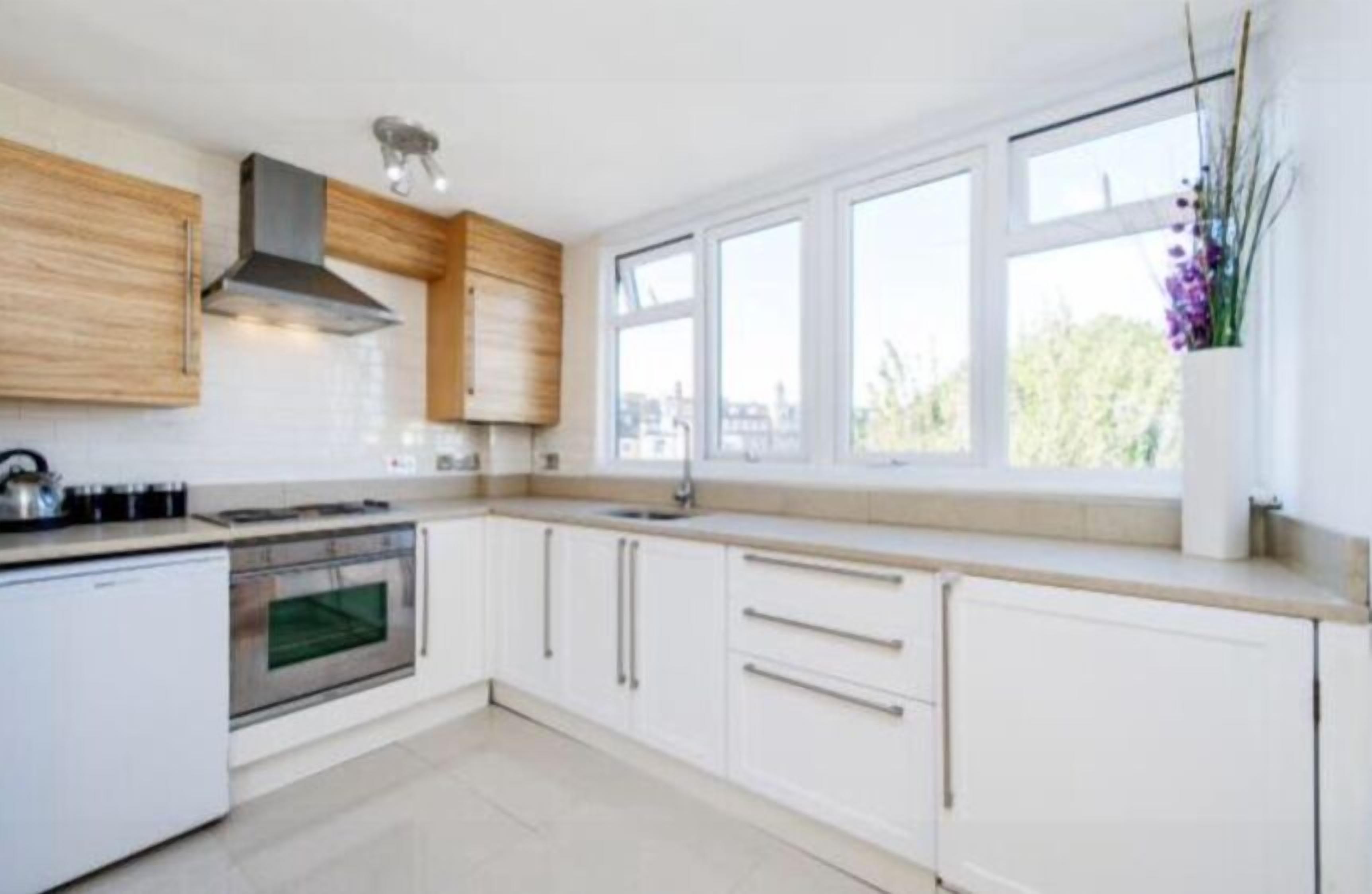 A modern kitchen with white cabinets, a built-in oven, and a window with a view of greenery.