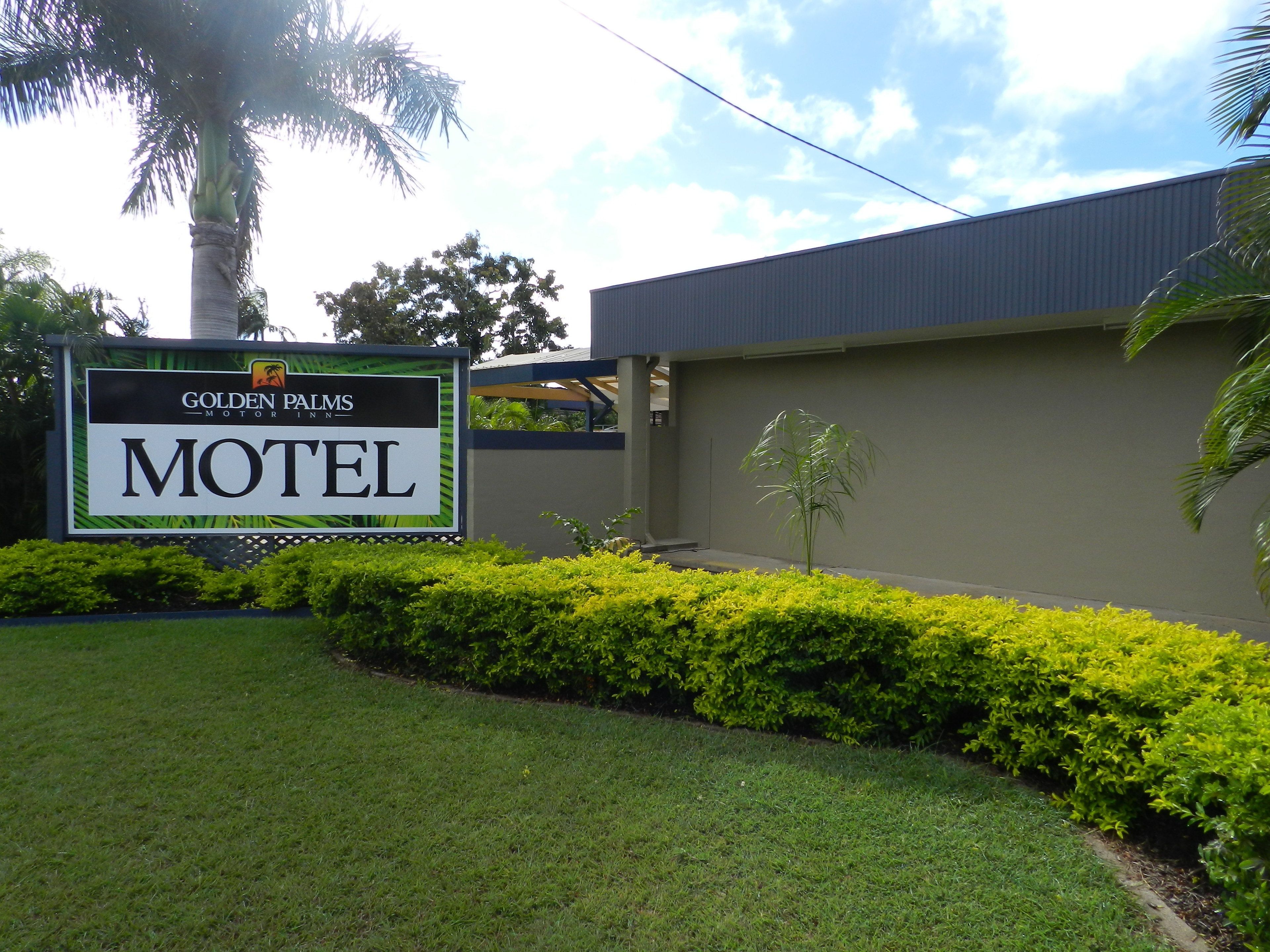 Letrero de motel con la leyenda 'Golden Palms Motor Inn' y 'Motel', rodeado de follaje cuidado y una palmera.