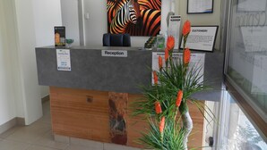 A reception desk with a sign labeled "Reception," a framed zebra painting on the wall, and a potted plant with orange flowers. - Golden Palms Motor Inn (Bundaberg)
