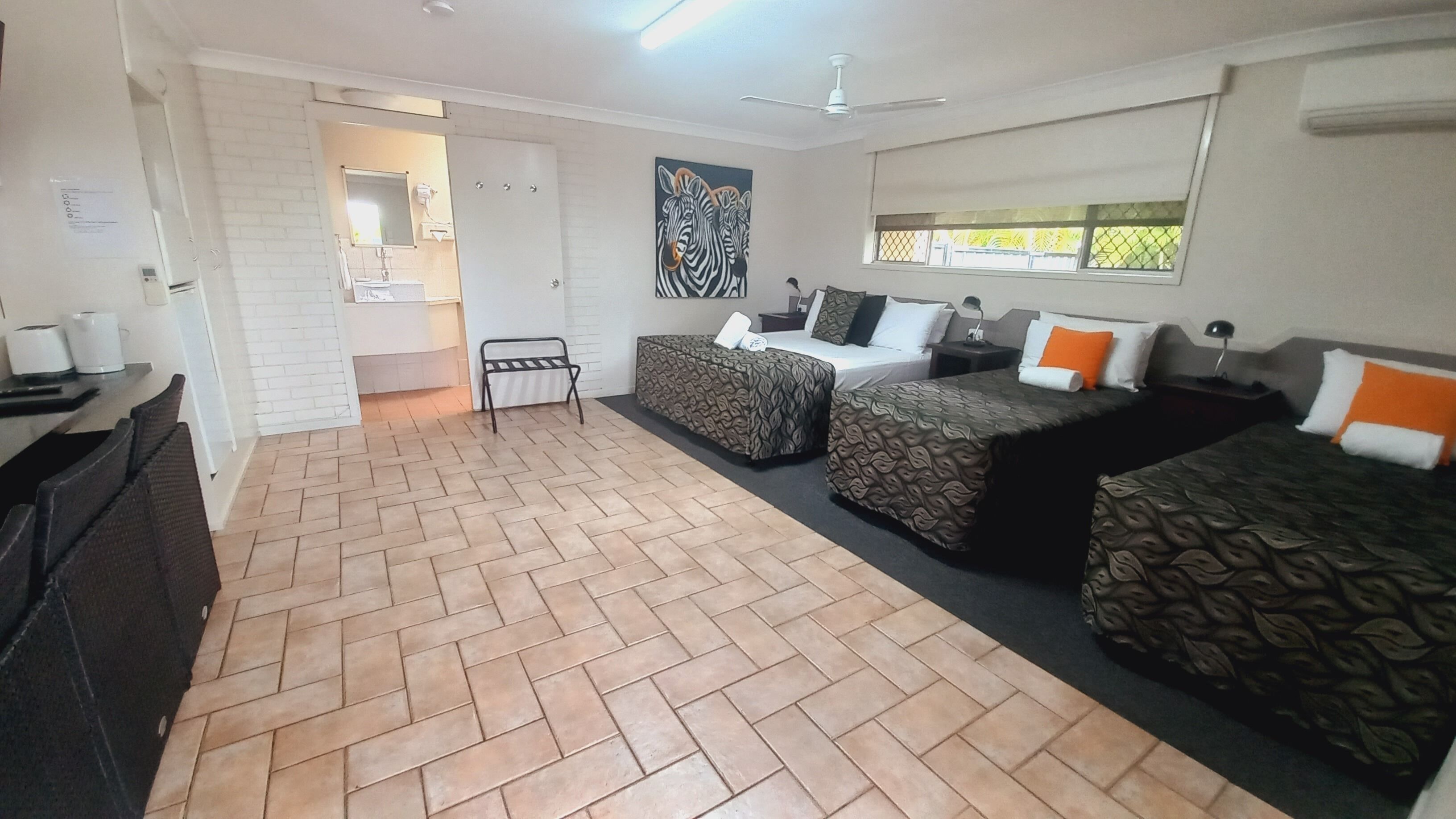 A hotel room with two beds, a bathroom, and a herringbone-patterned floor.