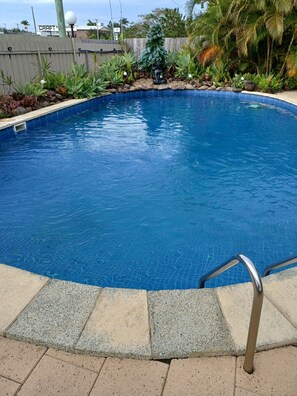 A swimming pool with a tiled edge, surrounded by a stone border and a wooden fence.