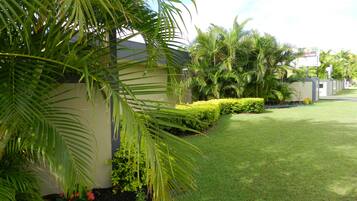 A well-maintained garden with palm trees, neatly trimmed hedges, and a grassy lawn.