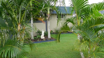 Un jardín cuidado con palmeras, una estatua y un edificio al fondo.