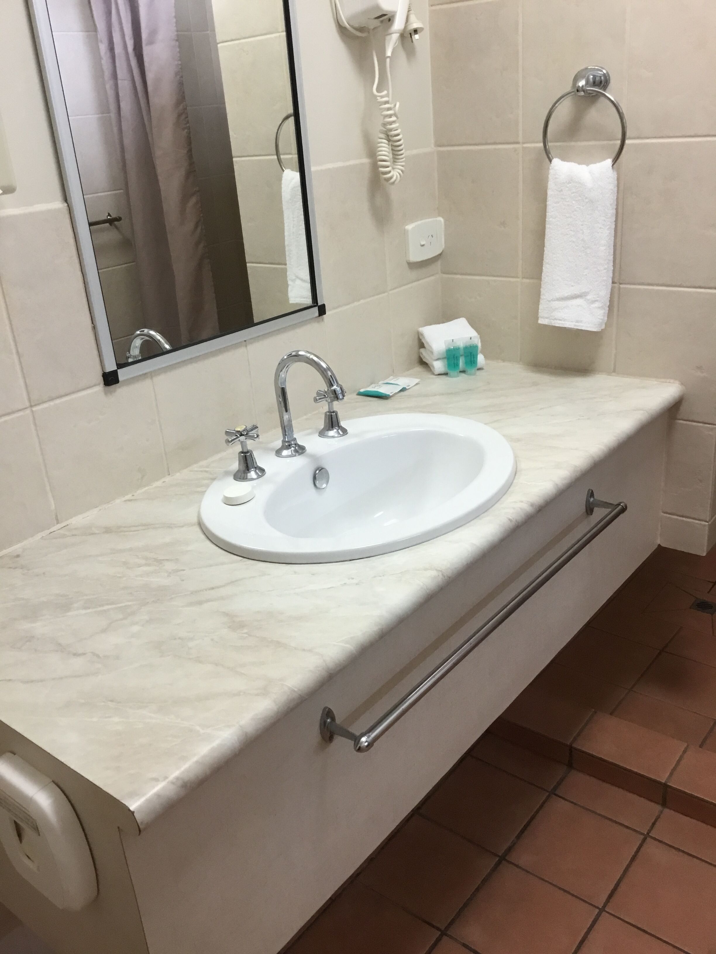 A bathroom with a white sink, a mirror, a towel ring, and a hairdryer on the wall.