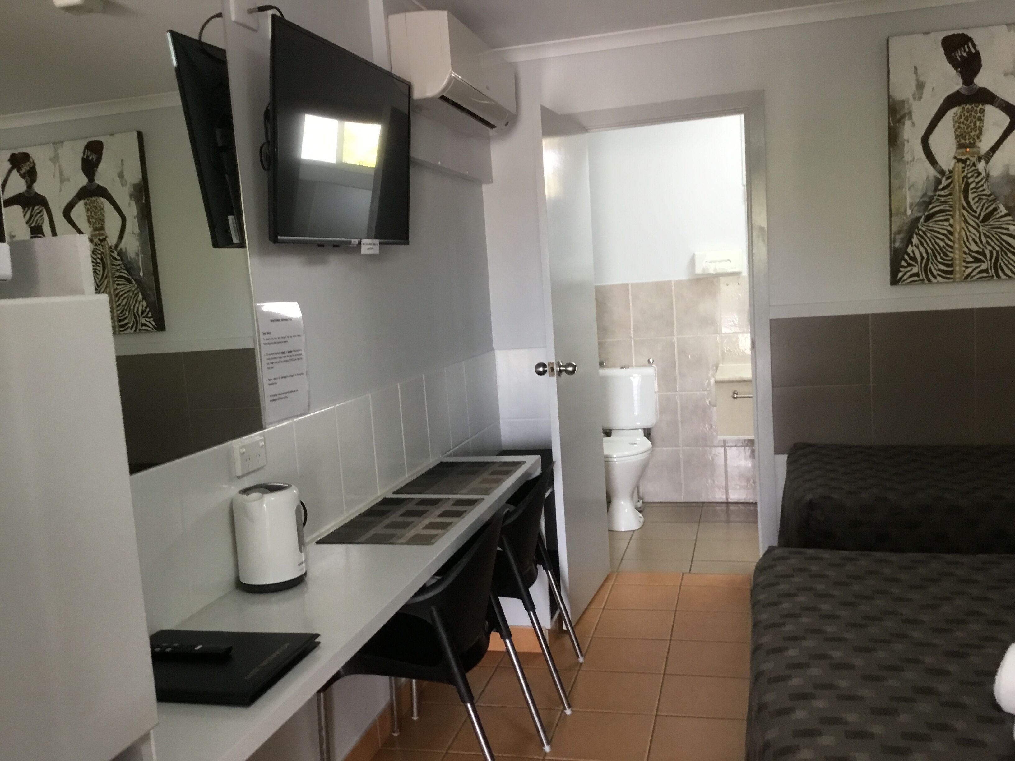 Habitación de hotel con cama, escritorio con computadora, televisión y baño visible a través de una puerta abierta.