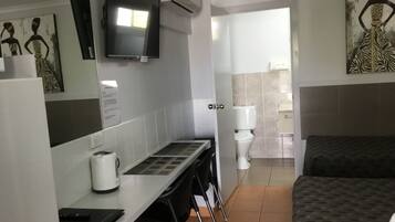 Habitación de hotel con cama, escritorio con computadora, televisión y baño visible a través de una puerta abierta.