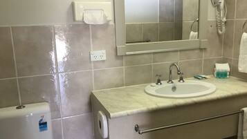 A bathroom with a sink, mirror, hair dryer, and hand dryer.