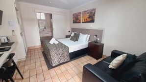 A hotel room with a bed, a desk, a chair, a sofa, a nightstand, and a painting on the wall. - Golden Palms Motor Inn (Bundaberg)