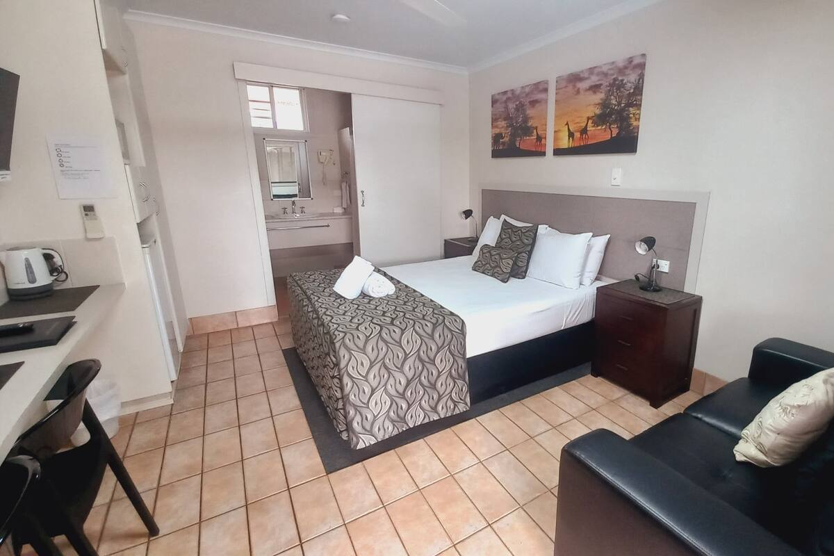 Quarto de hotel com cama, escrivaninha, cadeira, sofá, mesa de cabeceira e um quadro na parede.