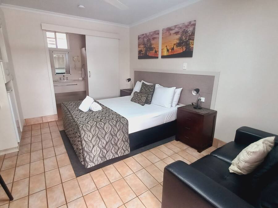 A hotel room with a bed, a desk, a chair, a sofa, a nightstand, and a painting on the wall.