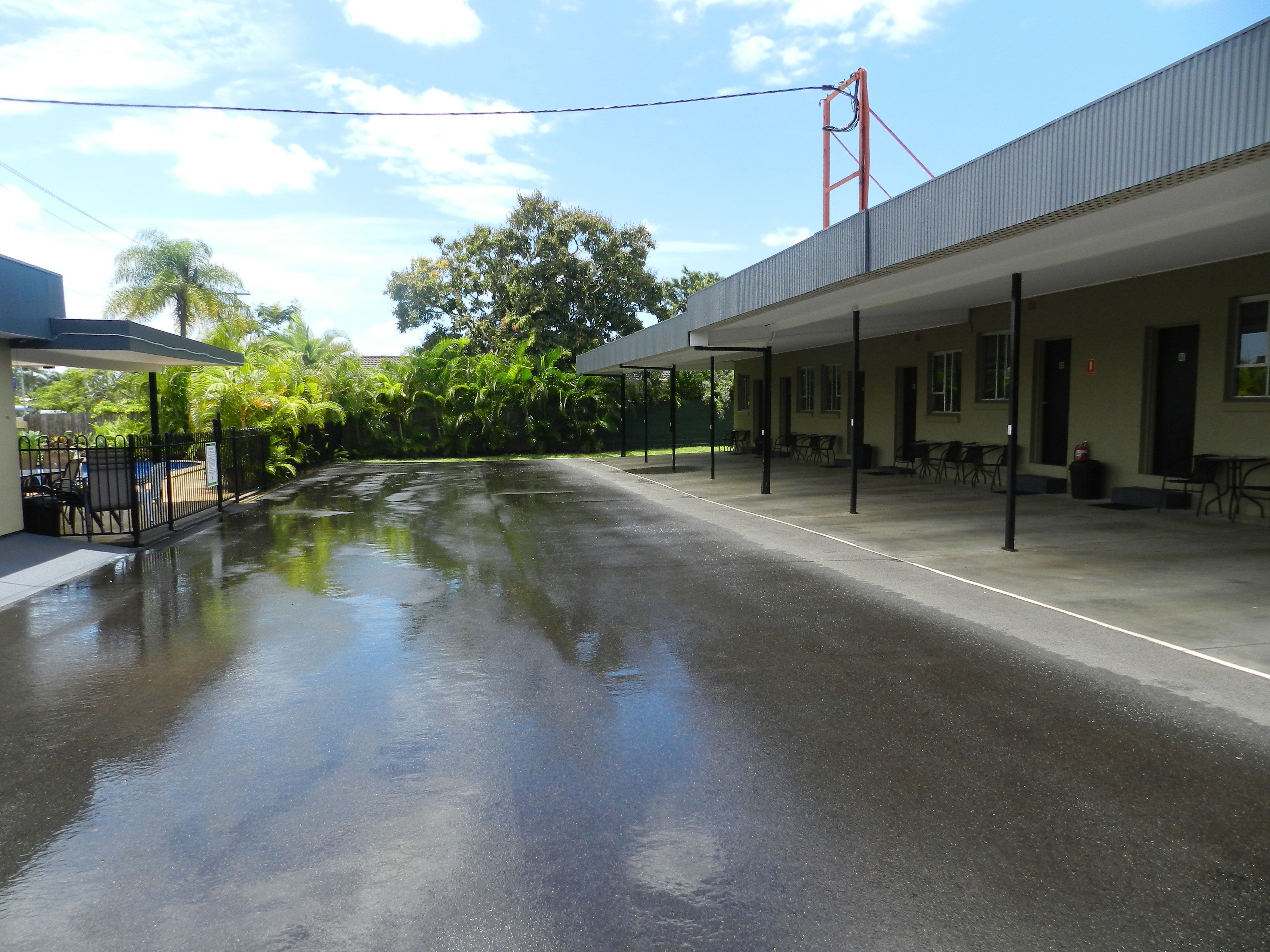 A covered outdoor area with a wet pavement, a building with a flat roof, and a red structure in the background.