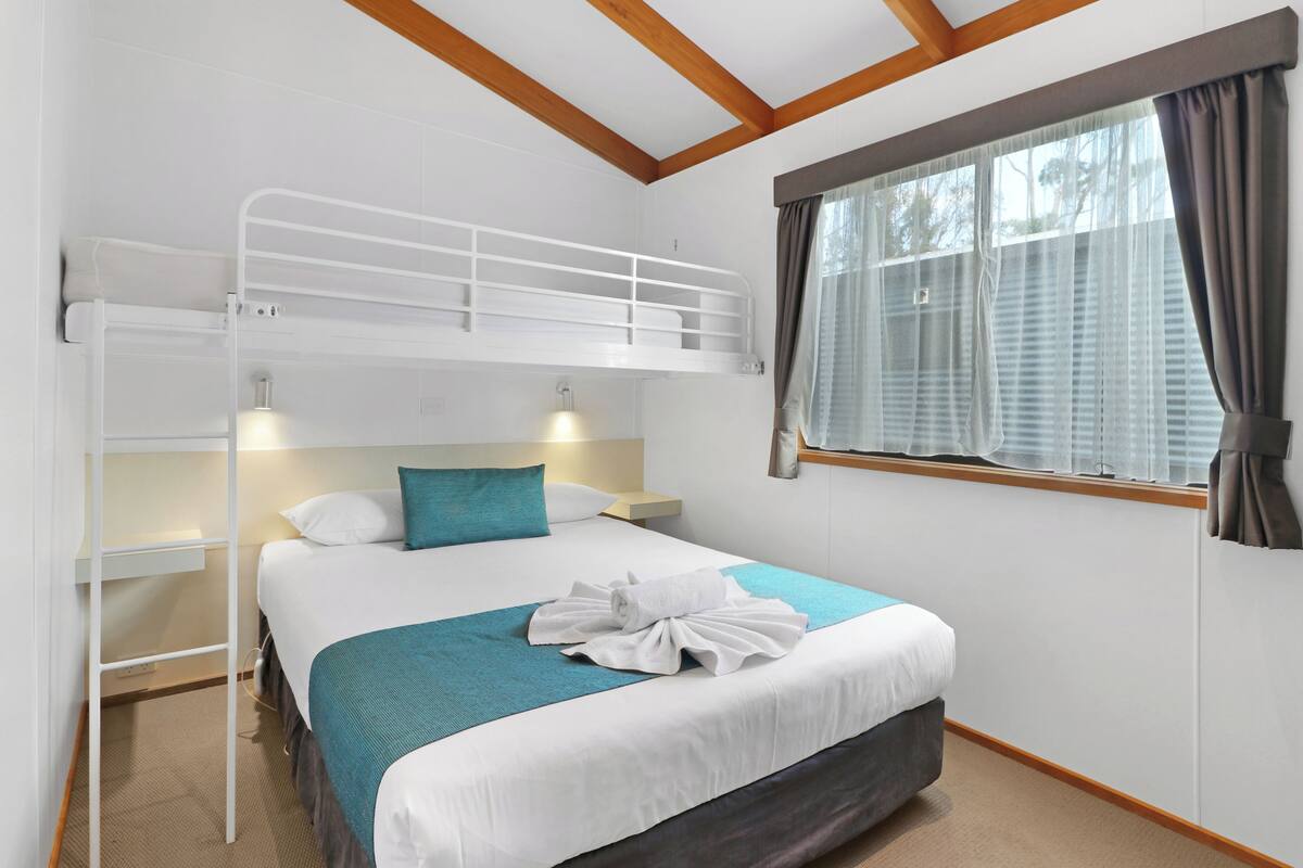 Une chambre avec un lit superposé, une fenêtre, une table de chevet et une serviette sur le lit.