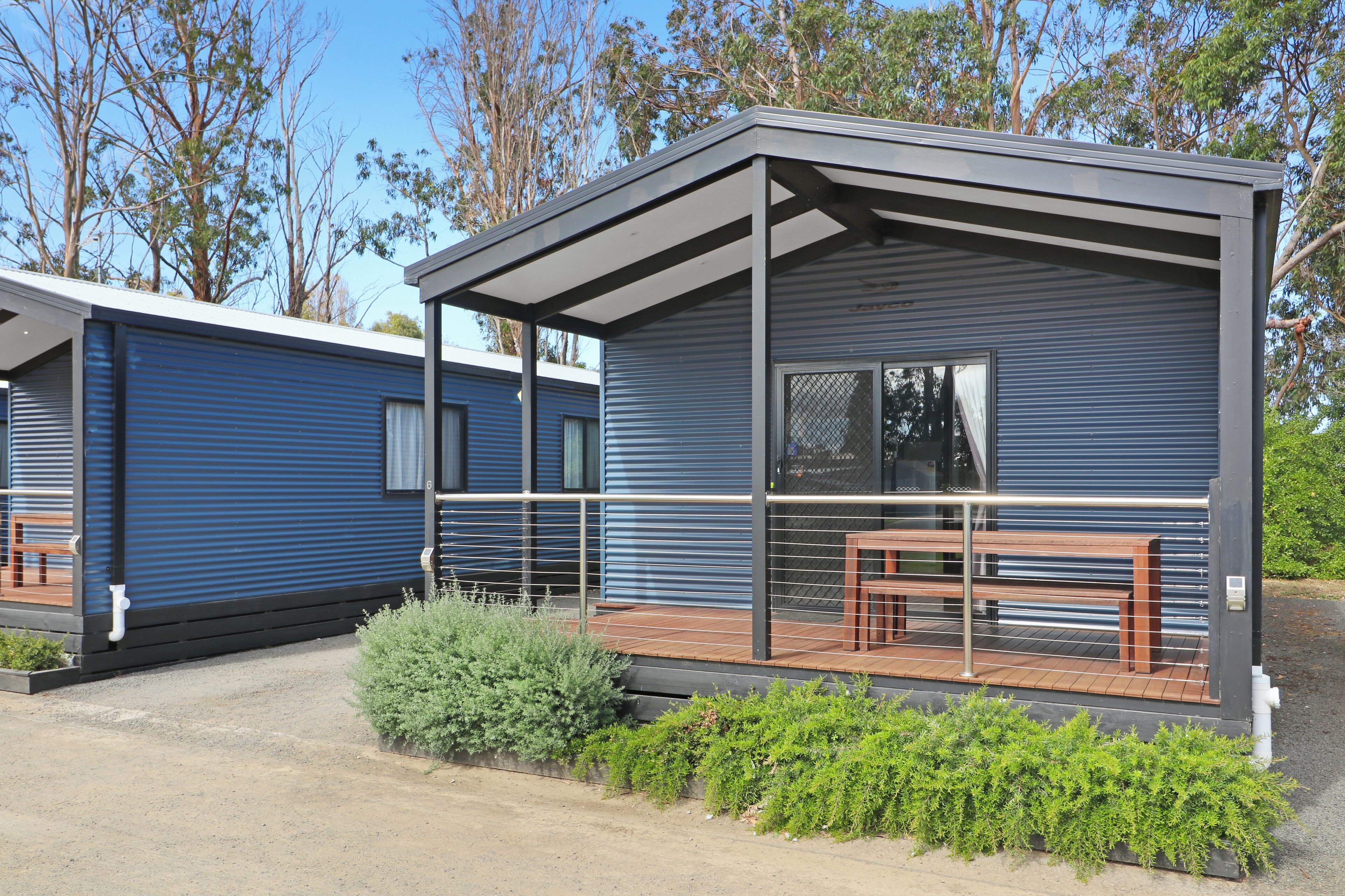 A modern, single-story mobile home with a covered porch, a small garden area, and a bench.
