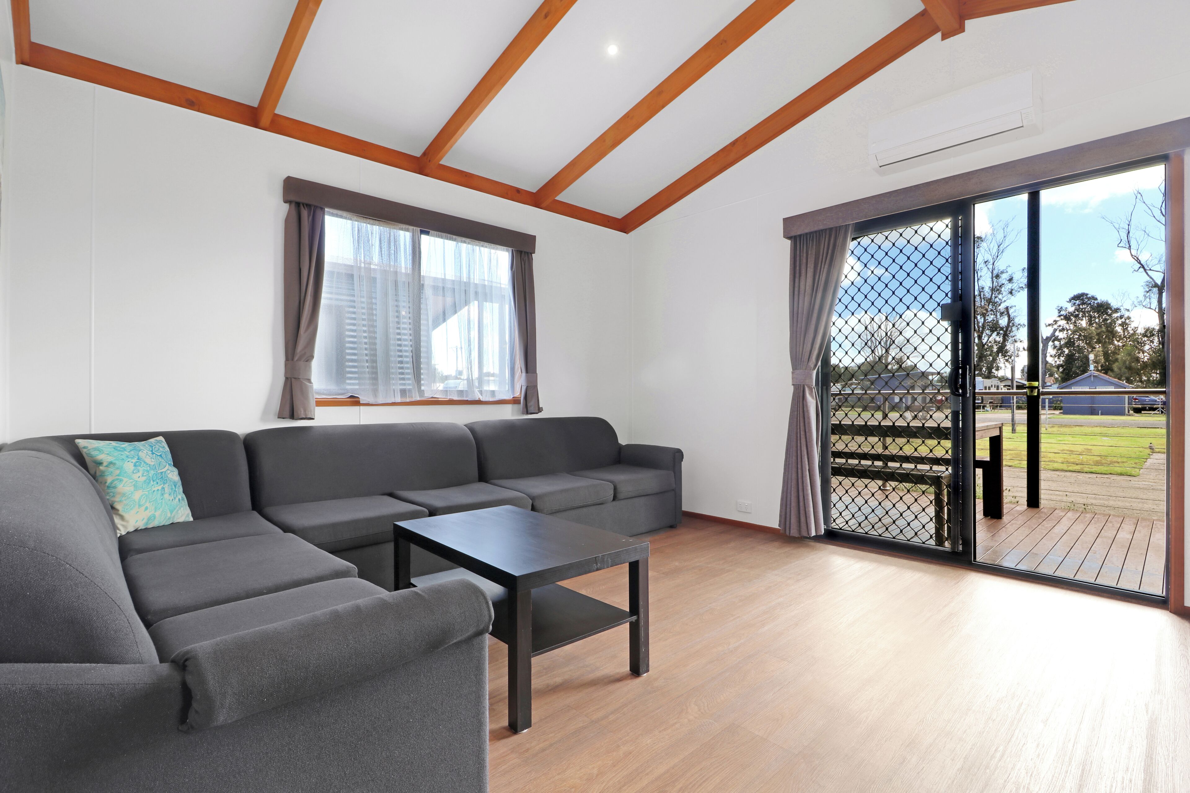 Ein modernes Wohnzimmer mit Ecksofa, einem kleinen Tisch und einer Schiebetür zu einer Terrisse.