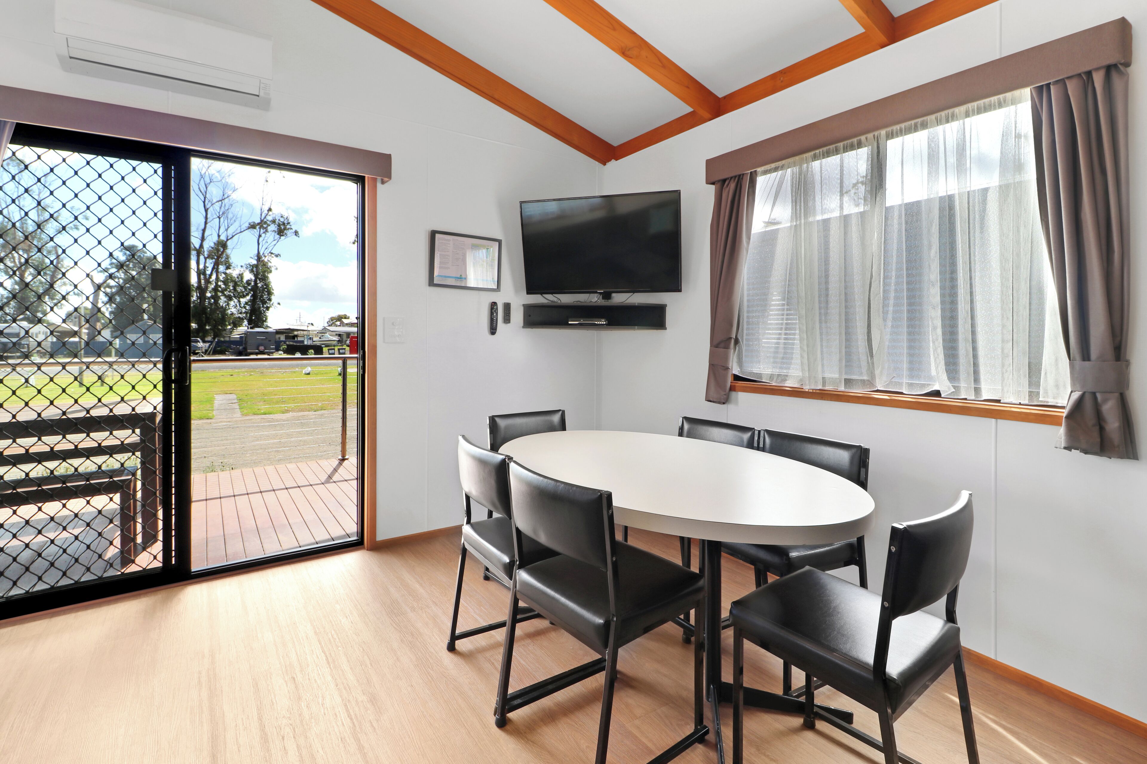 A room with a large window, a flat-screen TV, a round table with chairs, and a door leading outside.