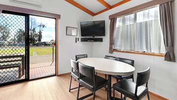 Ein Zimmer mit großem Fenster, einem Flachbildfernseher, einem runden Tisch mit Stühlen und einer Tür, die nach draußen führt.
