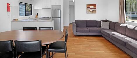 Una cocina moderna con armarios blancos, una mesa de comedor con sillas y un sofá seccional gris en una sala de estar con un ventanal grande.