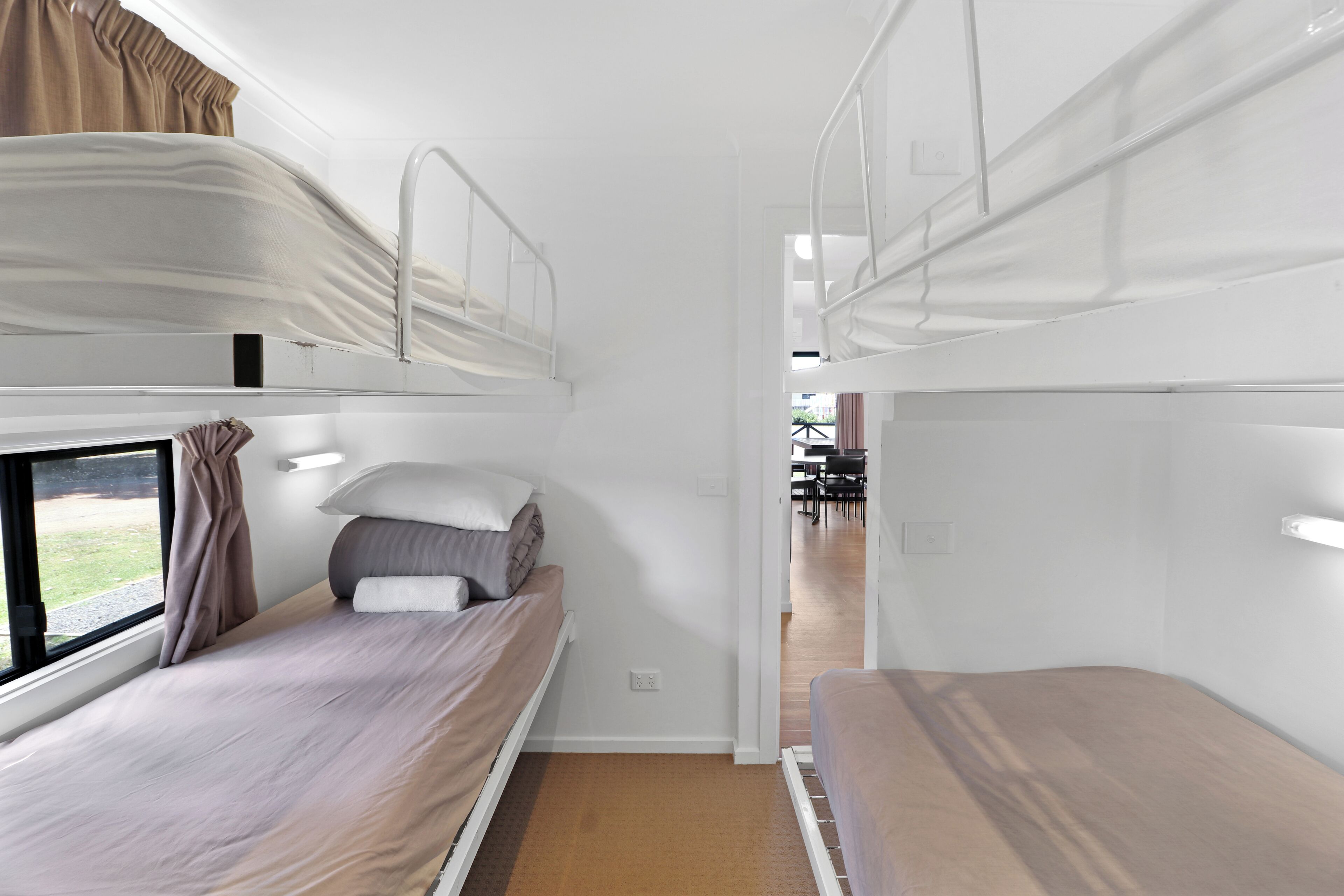 A train compartment with two bunk beds, a window with curtains, and a table in the adjacent room.