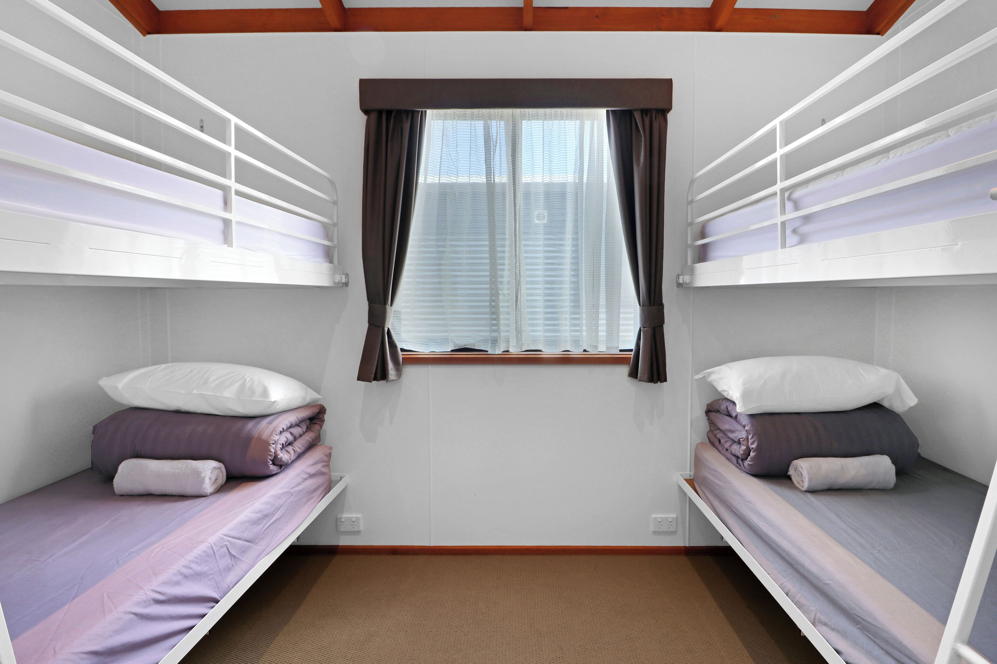 A room with bunk beds, a window with curtains, and a wooden ceiling.