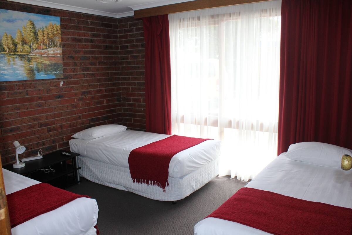 A hotel room with two beds, a painting on the wall, a brick wall, and a window with curtains.