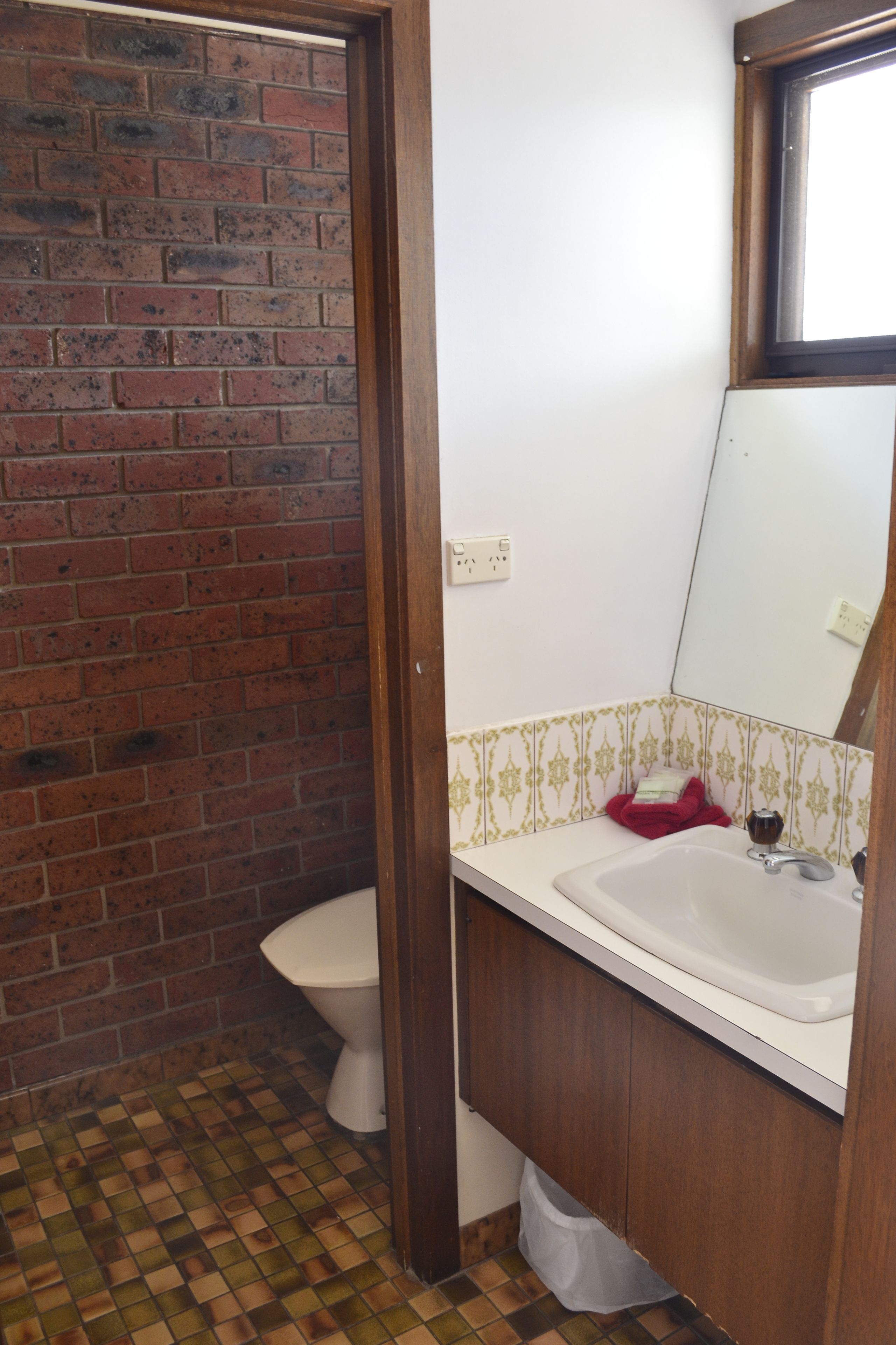 A bathroom with a white sink, a mirror, and a toilet. There is a red towel hanging on the wall. The floor has a checkered pattern.