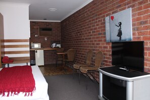 A hotel room with a bed, a TV, a desk with a computer, and a brick wall.
