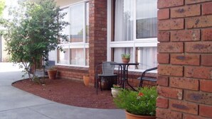 A brick building with large windows, a small patio area with a table and chairs, and potted plants. - Kardinia Park Motel (Newtown)