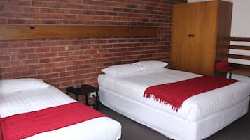 A room with two beds, a wooden wardrobe, and a brick wall.