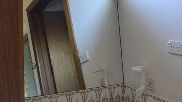 A bathroom with a white sink, two faucets, and a mirror above it. There is a red soap dish and a white towel holder on the wall.