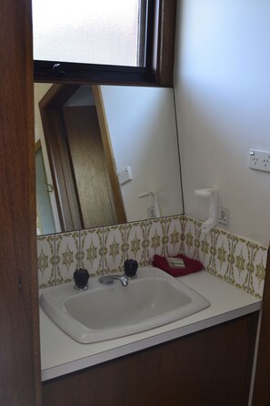 A bathroom with a white sink, two faucets, and a mirror above it. There is a red soap dish and a white towel holder on the wall.