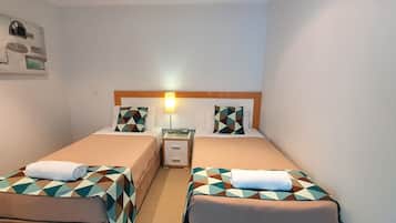 A hotel room with two beds, each with a geometric-patterned bedspread and matching pillows. There is a nightstand with a lamp between the beds, and a small drawer.