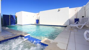 Une piscine dont le bord est recouvert de carreaux bleus et blancs, entourée de murs blancs et agrémentée d’un bac à fleurs bleu.