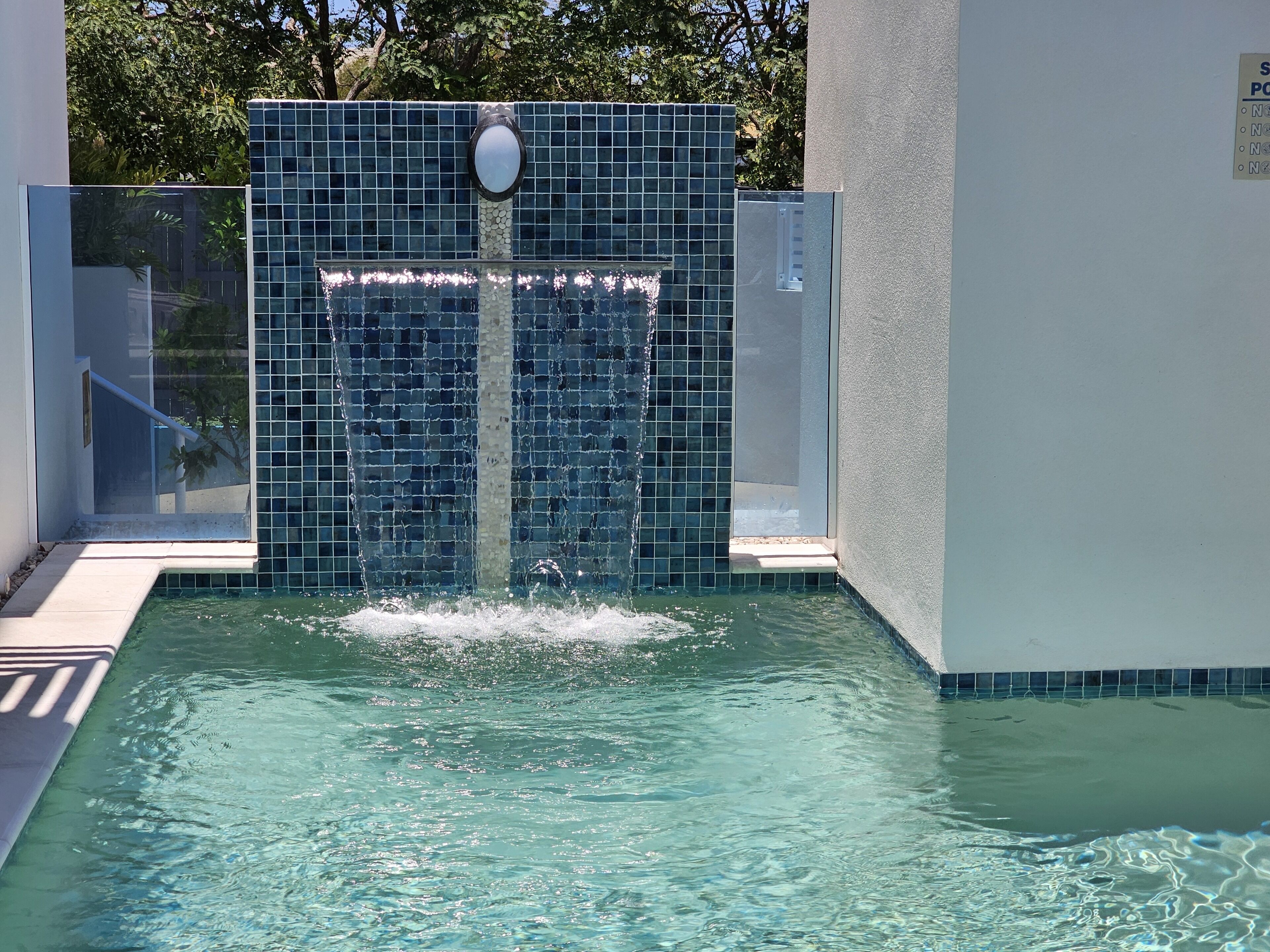 A swimming pool with a tiled wall and a water feature.
